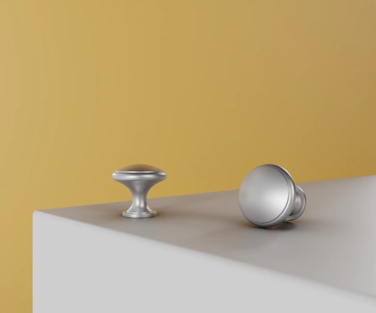 Zwei silberne Zink-Knäufe vom Typ KB-ZI-10053 auf einer weißen Fläche vor gelbem Hintergrund.