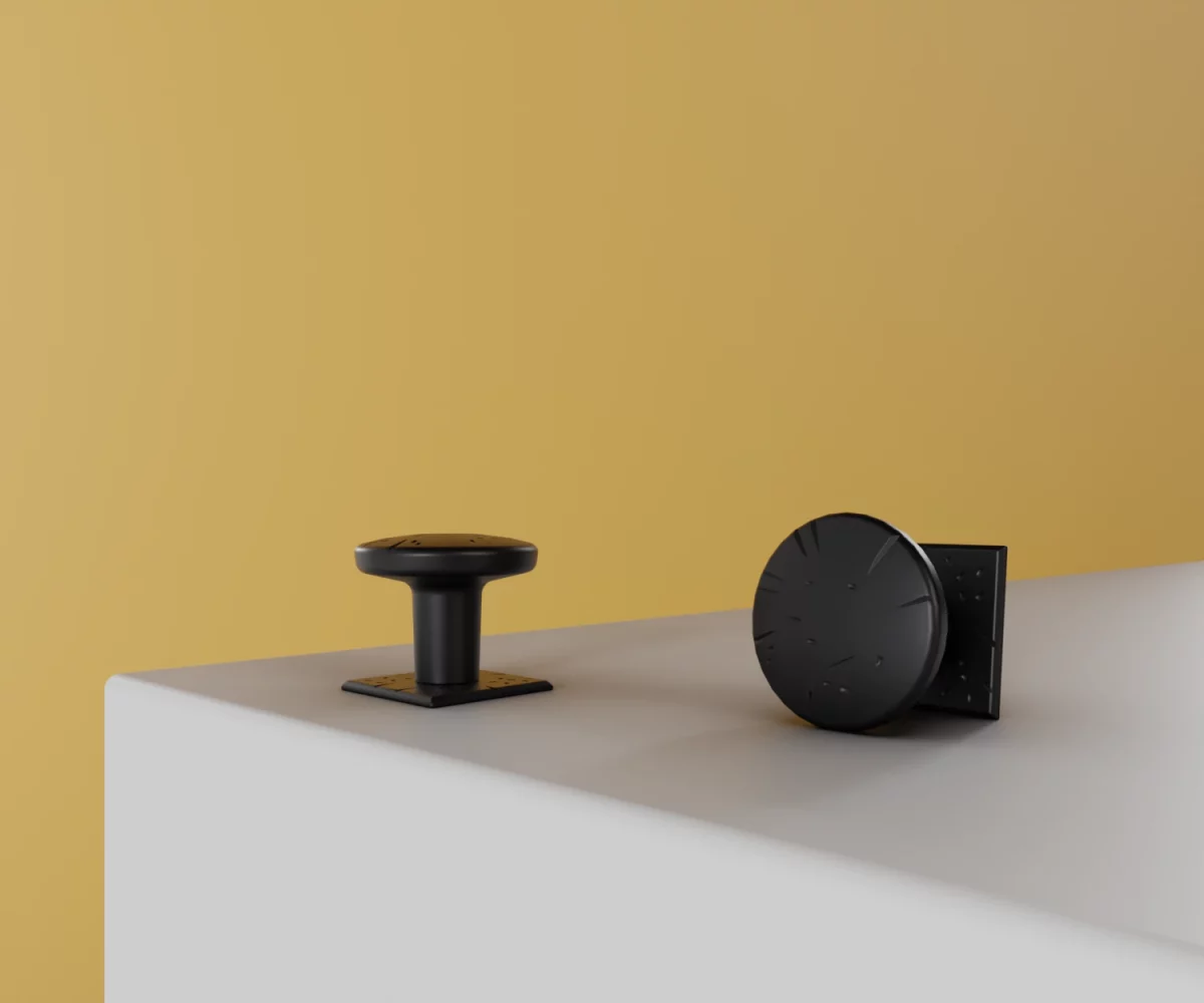 Zwei mattschwarze Zink-Knäufe vom Typ KB-ZI-10062 auf einer weißen Fläche vor gelbem Hintergrund.