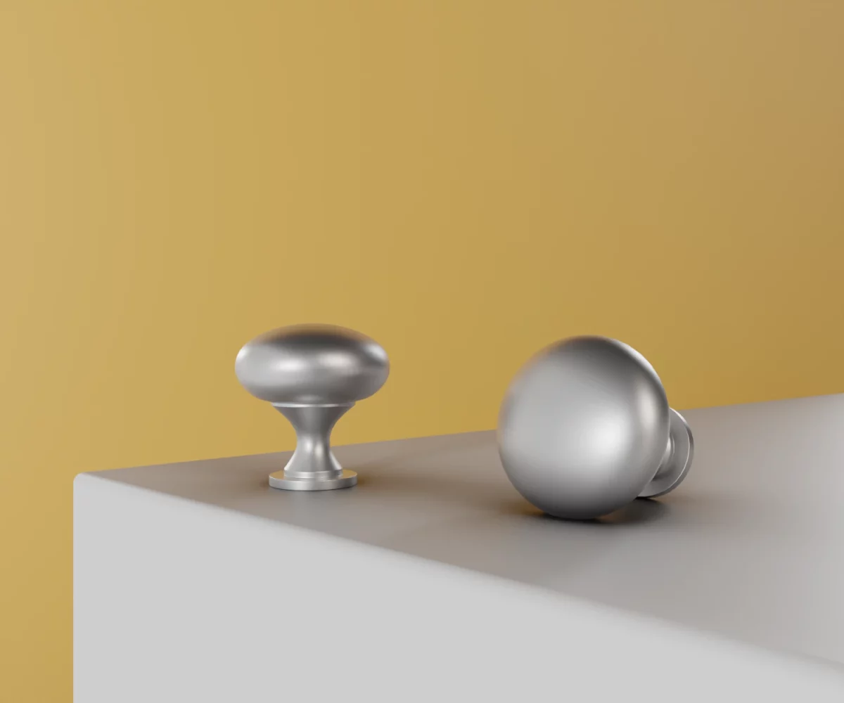 Zwei silberne Zink-Knäufe vom Typ KB-ZI-11003 auf einer weißen Fläche vor gelbem Hintergrund.