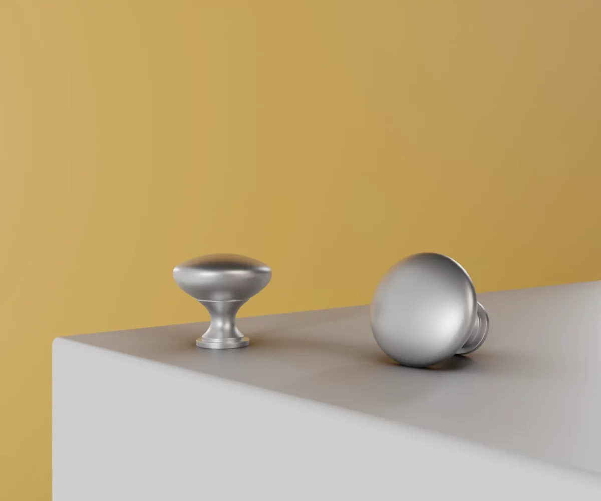 Zwei silberne Zink-Knäufe vom Typ KB-ZI-11006 auf einer weißen Fläche vor gelbem Hintergrund.