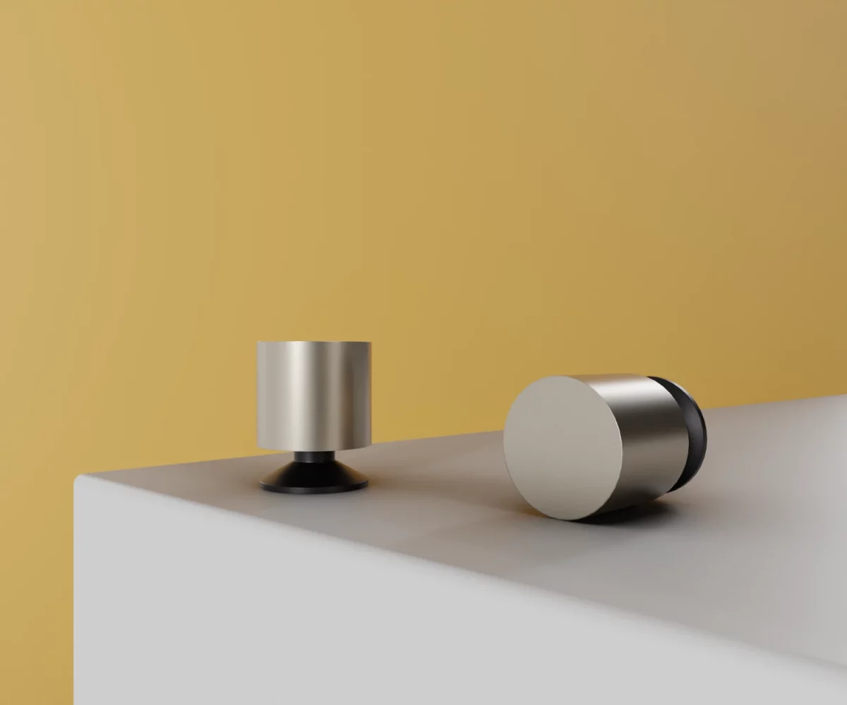 Zwei silberne Zink-Knäufe mit mattschwarzer Basis vom Typ KB-ZI-19031 auf einer weißen Fläche vor gelbem Hintergrund.