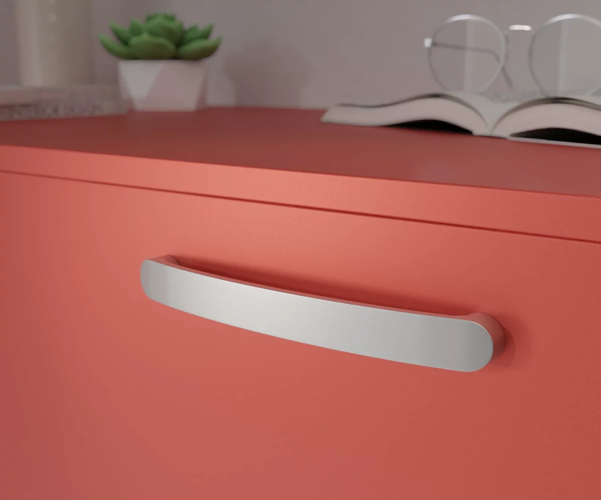 Silberfarbener Aluminium-Möbelgriff HA-AD-10023 mit sanft gerundeter Form und ergonomisch geschwungener Linienführung. Die Enden sind abgerundet und der Griff ist leicht nach außen gewölbt. Der Griff ist mittig auf einer korallenroten Schublade montiert dargestellt. Im Hintergrund unscharf dargestellt, befinden sich auf der rechten Seite ein aufgeschlagenes Buch mit einer Brille, die auf diesem Buch liegt. Auf der linken Seite befindet sich eine kleine grüne Pflanze in einem kleinen weißen Topf, links daneben eine hohe Vase und vor dieser Vase liegen zwei Bücher.