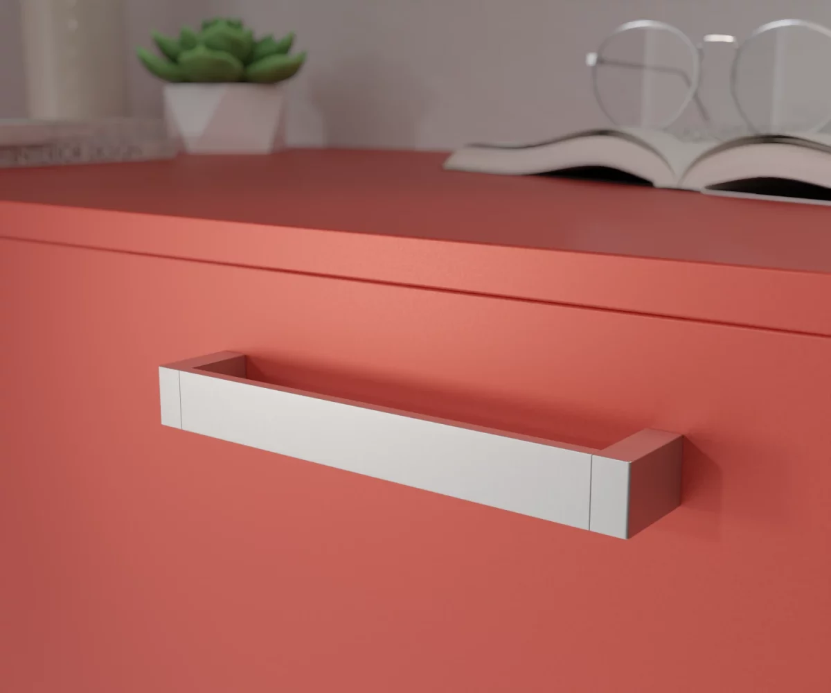 Silberfarbener Aluminium-Möbelgriff HA-AD-10027 mit glatter, geradliniger Oberfläche und modern eckigem Design. Der Griff ist mittig auf einer korallenroten Schublade montiert dargestellt. Im Hintergrund unscharf dargestellt, befinden sich auf der rechten Seite ein aufgeschlagenes Buch mit einer Brille, die auf diesem Buch liegt. Auf der linken Seite befindet sich eine kleine grüne Pflanze in einem kleinen weißen Topf, links daneben eine hohe Vase und vor dieser Vase liegen zwei Bücher.
